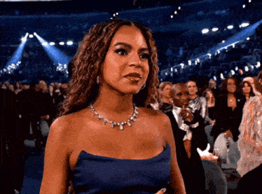 a woman in a blue dress and necklace is standing in front of a crowd at a concert .