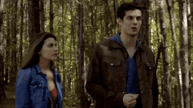 a man and a woman are standing in a forest .