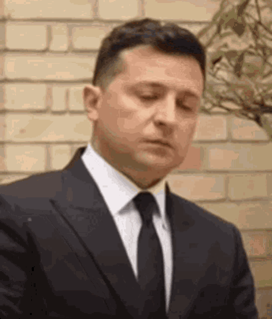 a man in a suit and tie is looking down with his eyes closed .