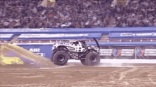 a monster truck is doing a trick on a dirt track in front of a crowd .