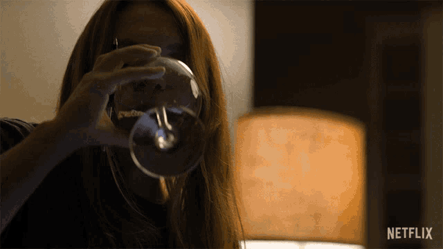 a woman holds a glass in front of her face with a netflix logo in the corner