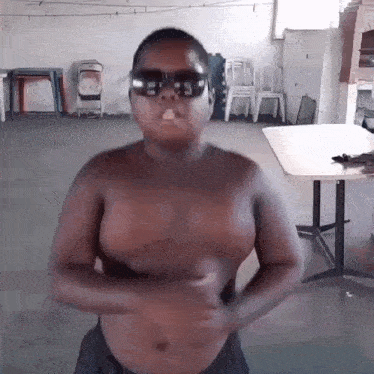 a shirtless man wearing sunglasses is standing in a room with chairs .