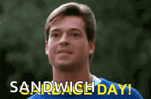 a man in a blue sweater is smiling and says `` sandwich day '' .