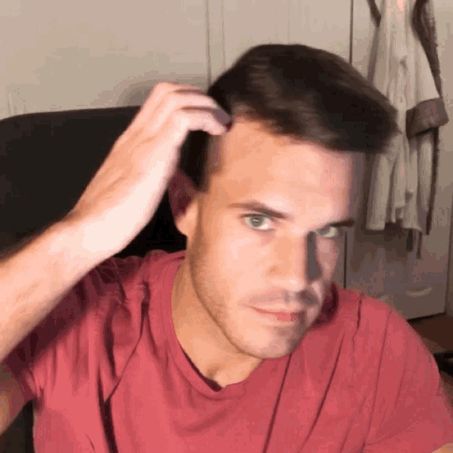 a man in a red shirt is touching his hair with his hand