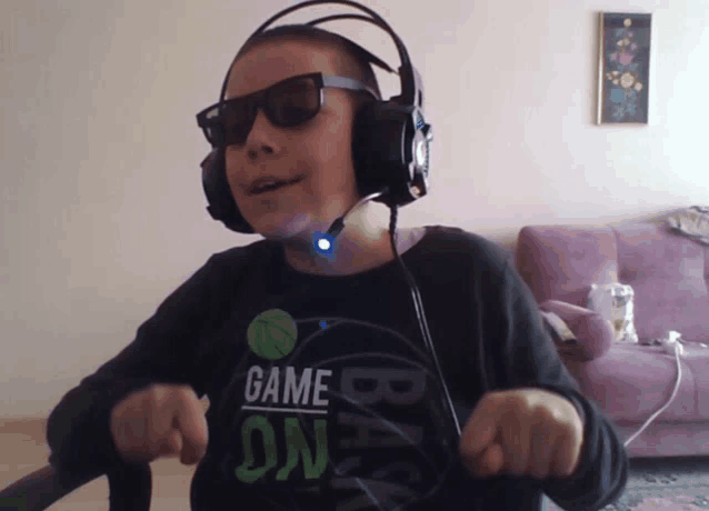 a young boy wearing headphones and sunglasses has a shirt that says game on