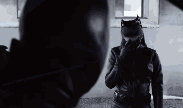 a man and a woman are standing next to each other . the woman is wearing a cat mask and covering her face .