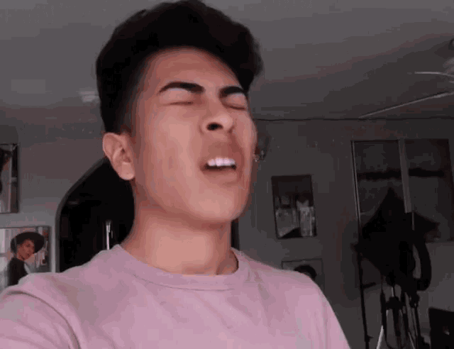 a young man in a pink shirt is making a face