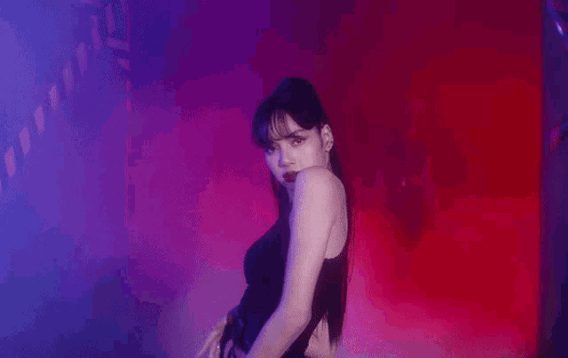 a woman in a black dress is dancing in a dark room with purple lights .