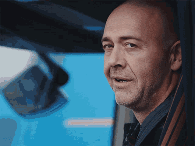 a bald man with a beard is looking out of a car window