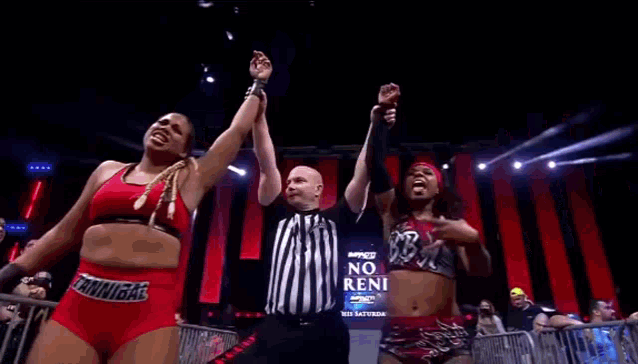two female wrestlers are standing next to each other on a stage holding hands with a referee .