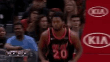 a man in a basketball jersey is sitting in the stands with his hands in the air .