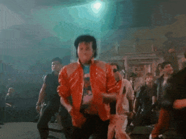 a man in a red jacket is dancing in front of a crowd in a dark room .