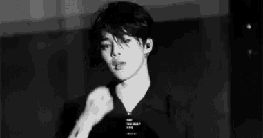 a black and white photo of a young man wearing a black shirt and earrings .