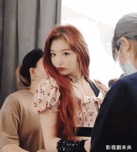 a woman with red hair is standing next to a woman wearing a face mask