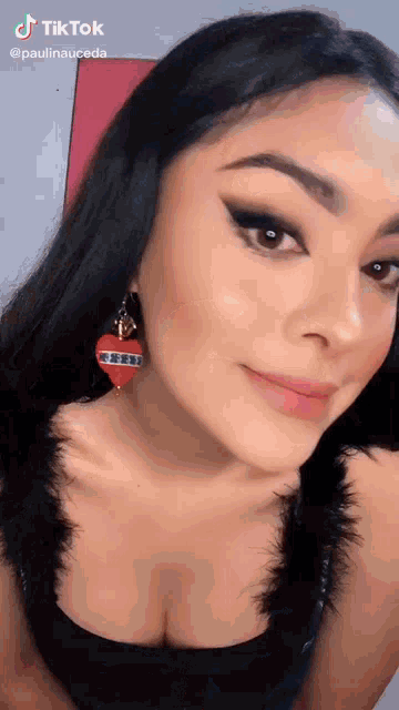 a woman wearing a black top and red heart shaped earrings is looking at the camera .