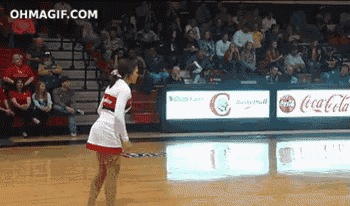 a cheerleader stands on a basketball court in front of coca-cola advertisements