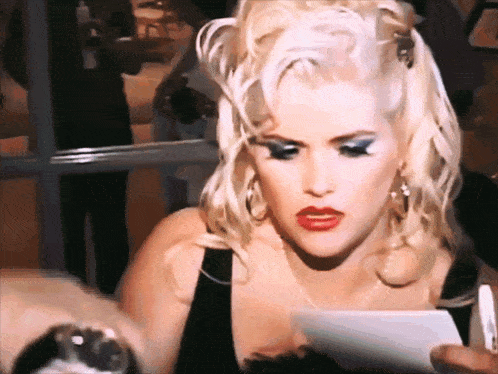 a woman with blonde hair and red lips is looking at something