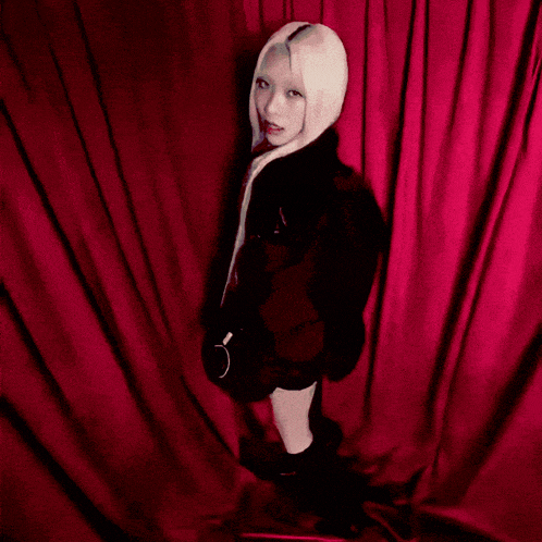 a woman with long blonde hair is standing in front of a red curtain with the name maya written on the bottom