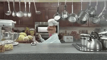 a muppet chef is standing in a kitchen with pots and pans hanging from the ceiling