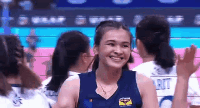 a woman in a blue tank top is smiling while standing in front of a volleyball net .