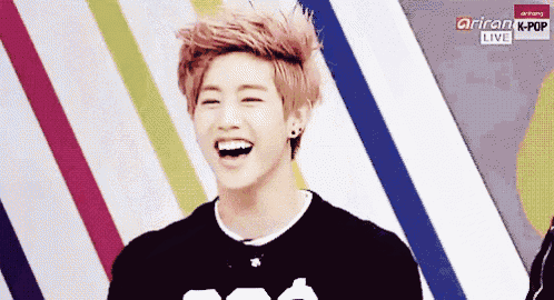 a young man with pink hair is laughing in front of a colorful background with the words arirang kpop live on the bottom