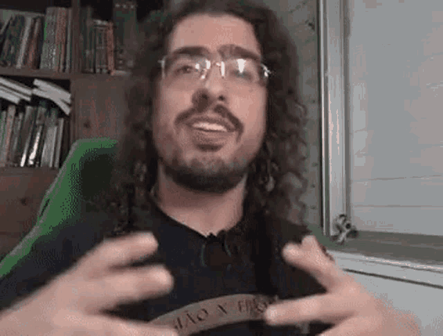 a man with long curly hair and glasses is sitting in a chair and making a funny face .