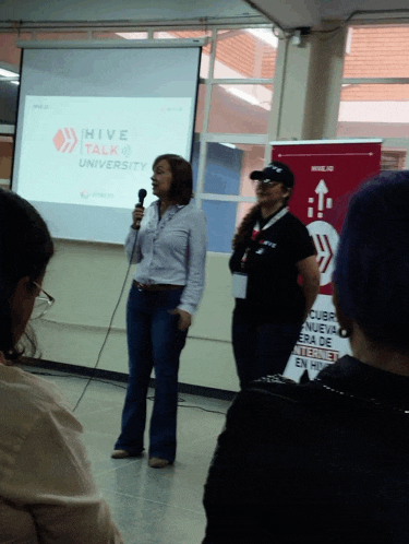 a woman stands in front of a hive talk university screen