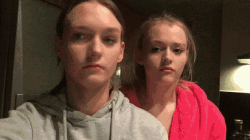 two girls are standing next to each other in a kitchen and looking at the camera .