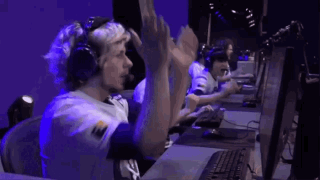 a group of people are sitting in front of computer monitors and raising their hands in the air .