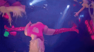 a woman in a pink bodysuit and red boots is doing a handstand on a stage .