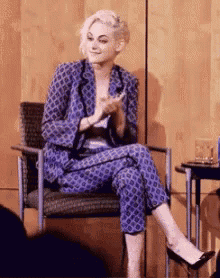 a woman in a blue suit is sitting in a chair and clapping .