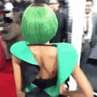 a woman with green hair is standing on a red carpet wearing a green dress .