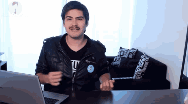 a man sitting at a desk with a laptop and a sticker on his jacket that says ' u '