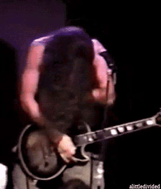 a man with long hair is playing a guitar and singing into a microphone with the words alittle divided below him
