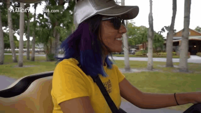 a woman with purple hair is driving a golf cart with the website platica.com behind her