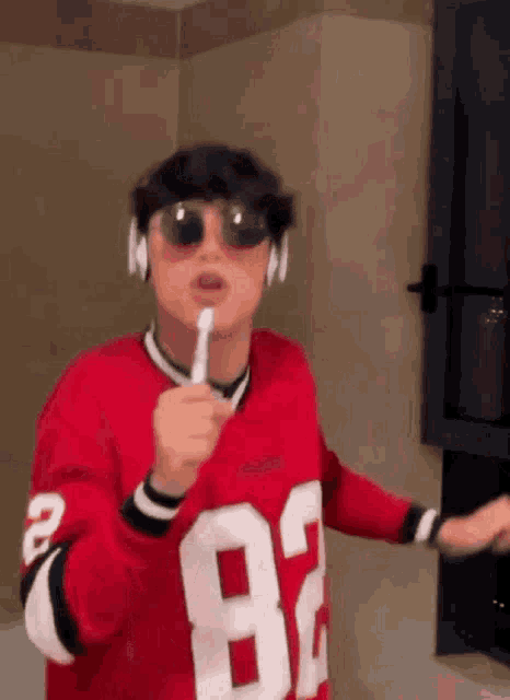 a young man wearing sunglasses and headphones is brushing his teeth .