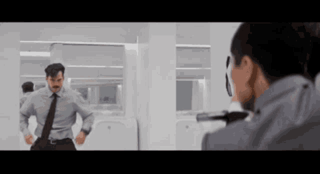 a man in a suit and tie is standing in front of a mirror while another man takes a picture of him .