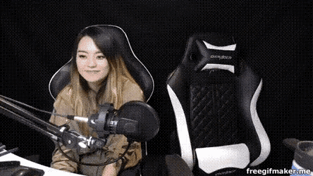 a woman is sitting in a gaming chair in front of a microphone and smiling .
