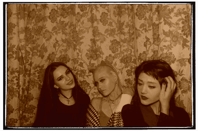 three women posing for a picture in front of a floral curtain