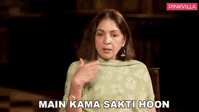 a woman in a green dress is sitting in a chair with the words main kama sakti hoon below her