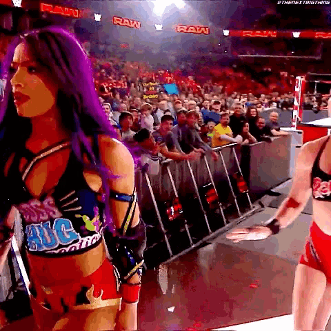 a woman with purple hair is standing in front of a crowd while wearing a shirt that says raw