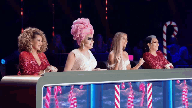 four drag queens are sitting at a table with candy canes on it