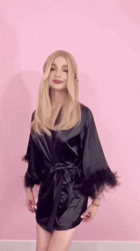 a woman in a black robe with feathers on the sleeves stands in front of a pink wall