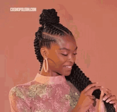 a woman with long braids in a bun is holding her hair .