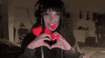 a woman wearing headphones making a heart with her hands