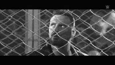 a black and white photo of a man behind a chain link fence with a w logo on the bottom