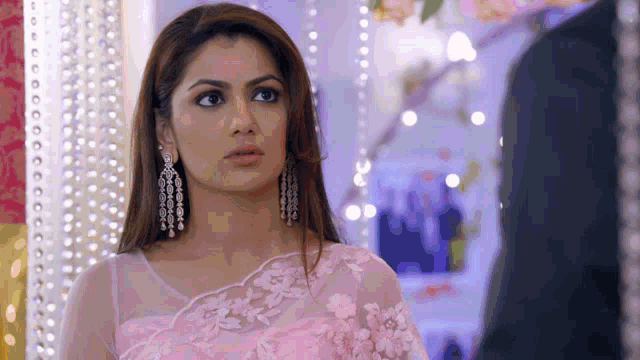 a woman wearing a pink saree and earrings is looking at a man in a suit .
