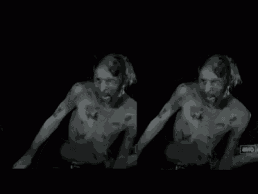 a man with tattoos on his chest is standing in the dark without a shirt on .