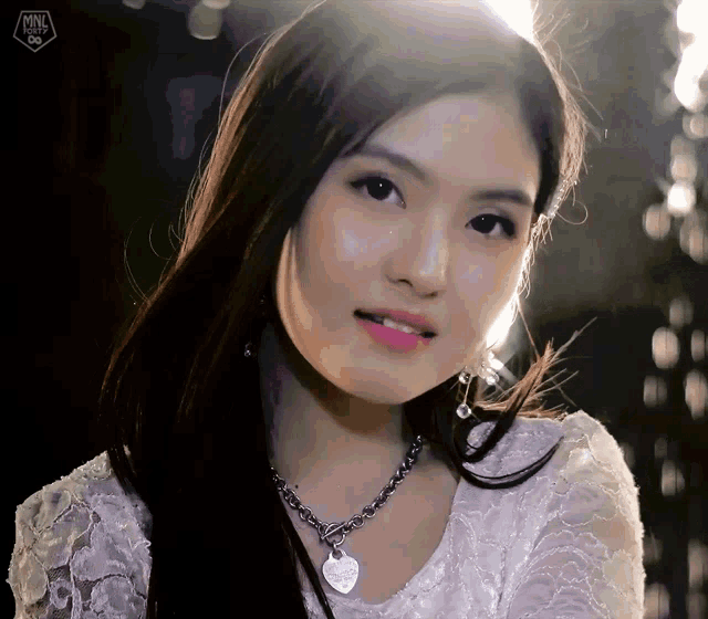 a woman wearing a white lace top and a necklace with a heart shaped pendant