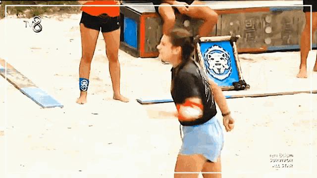 a woman is throwing a frisbee on a beach in front of a sign that says t8 on it